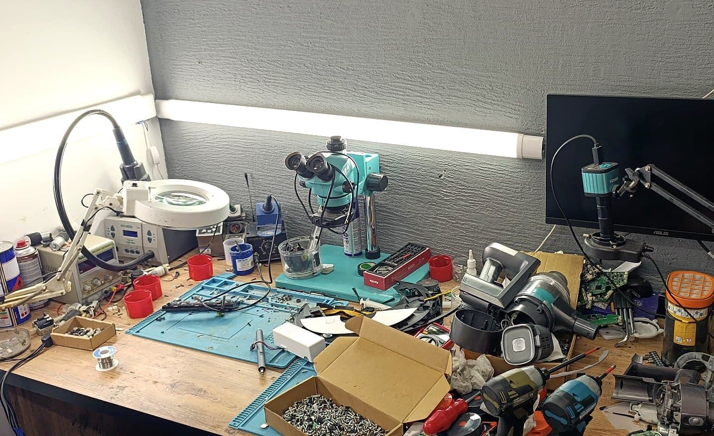 Onarım tezgâhının geniş görünümü: büyüteçli lamba, lehim istasyonları, stereo mikroskop ve antistatik mat